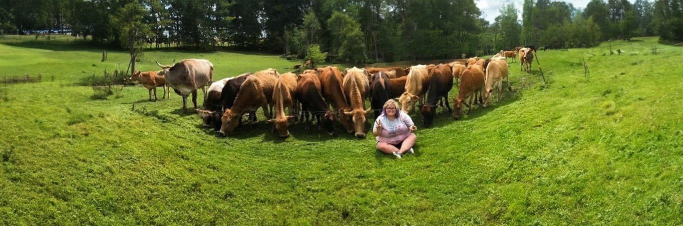 Heather, someone with NMOSD, sitting down in a field with her heard of cows.